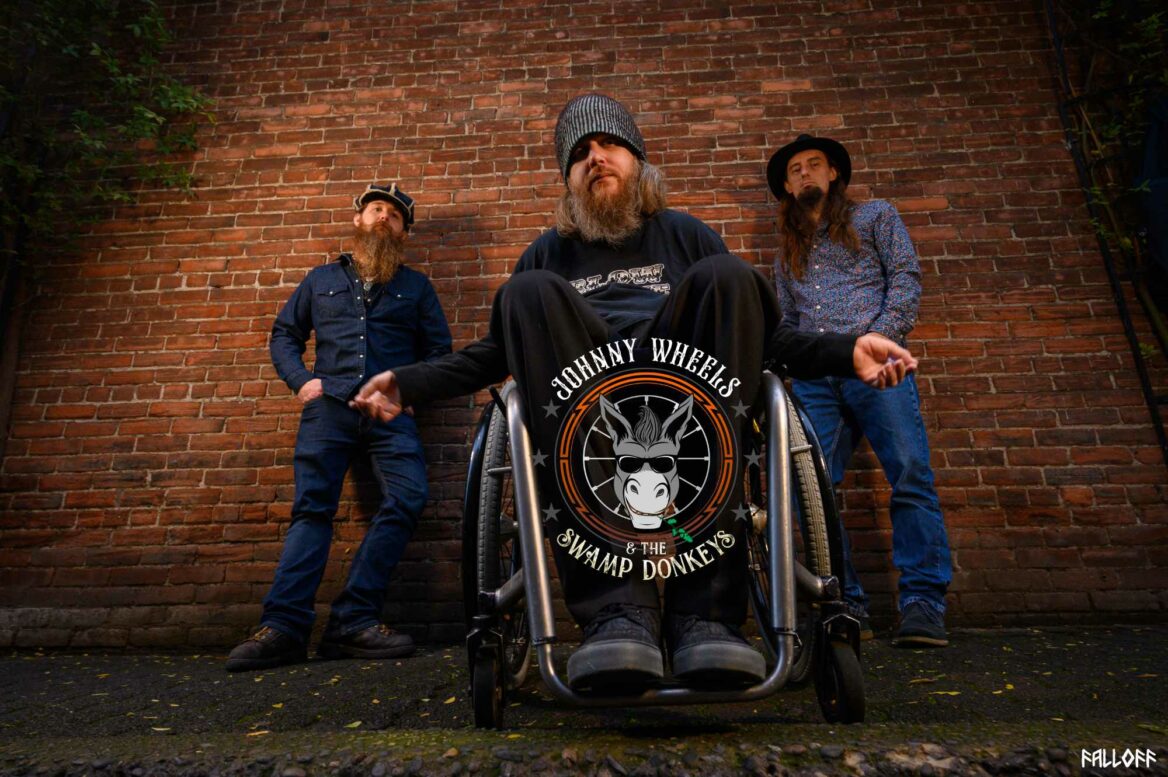 Johnny Wheels & The Swamp Donkeys promo picture featuring Johnny, Brandon and Taylor with a brick wall behind them, featuring the new round logo.